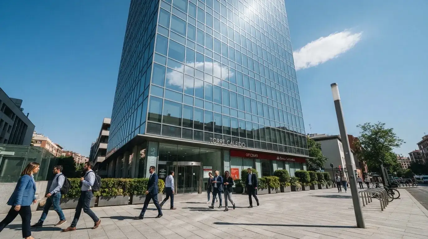 Edificio de oficinas moderno con fachada de cristal bajo un cielo despejado, gente caminando por la acera en una calle de ciudad.